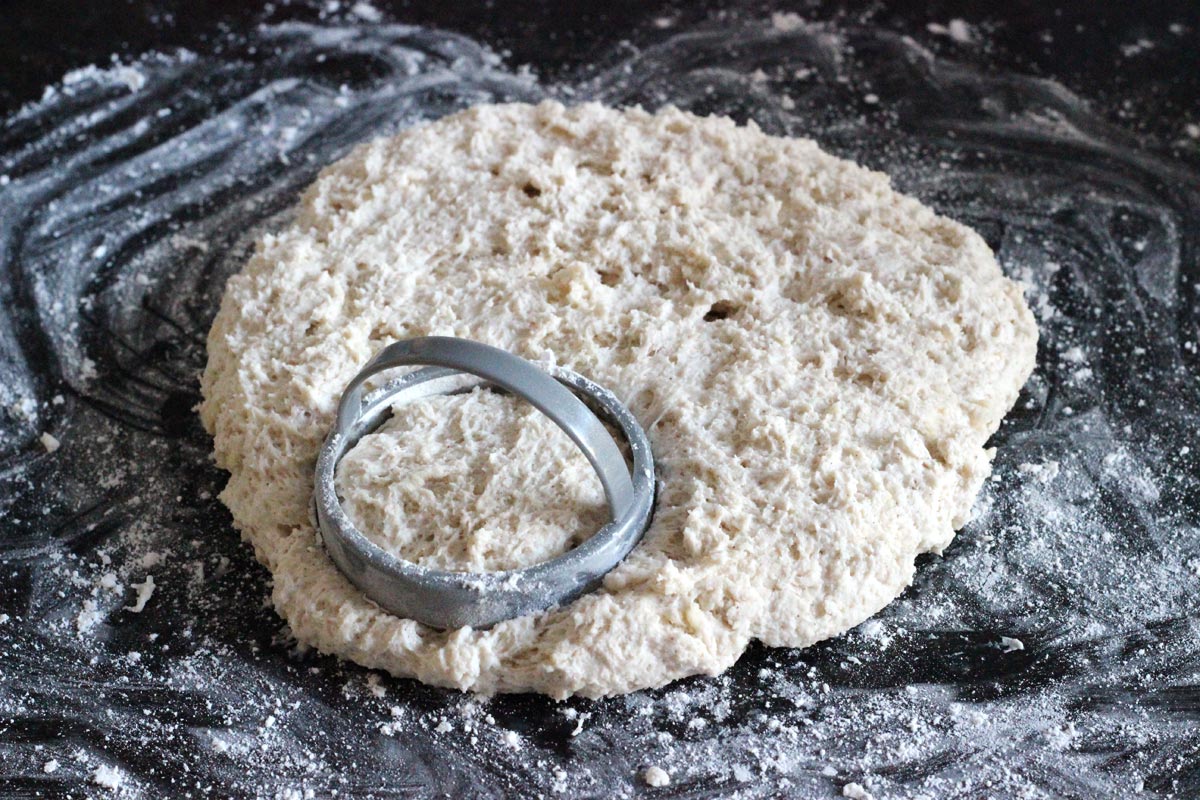 A biscuit cutter pressed into shaggy biscuit dough.