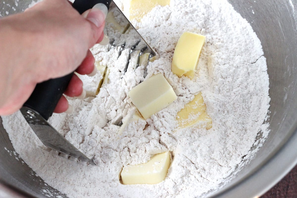 Hand using a pastry cutter to cut butter into biscuit ingredients.