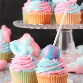 Close up of two cotton candy cupcakes with a tray of cupcakes in the background.