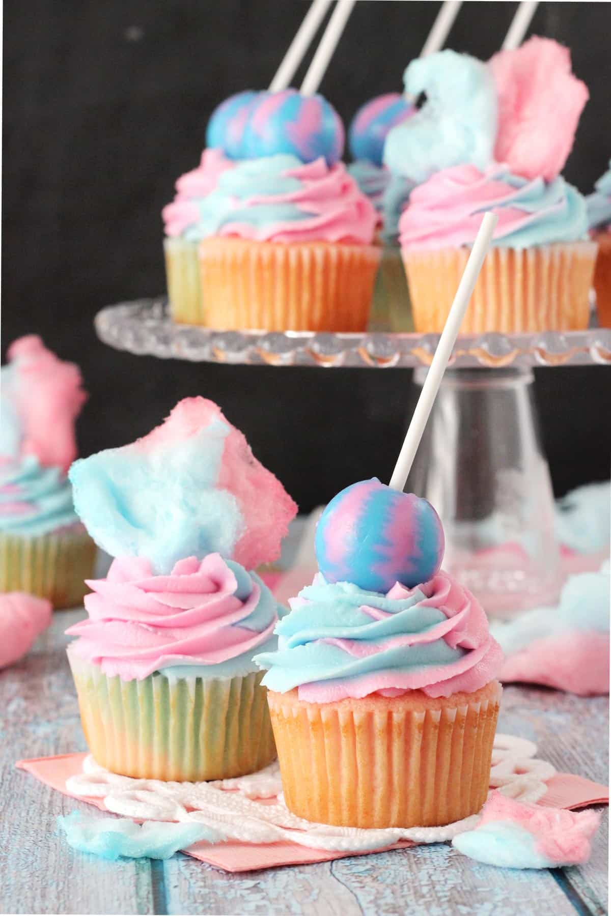 Close up of two cotton candy cupcakes with a tray of cupcakes in the background.