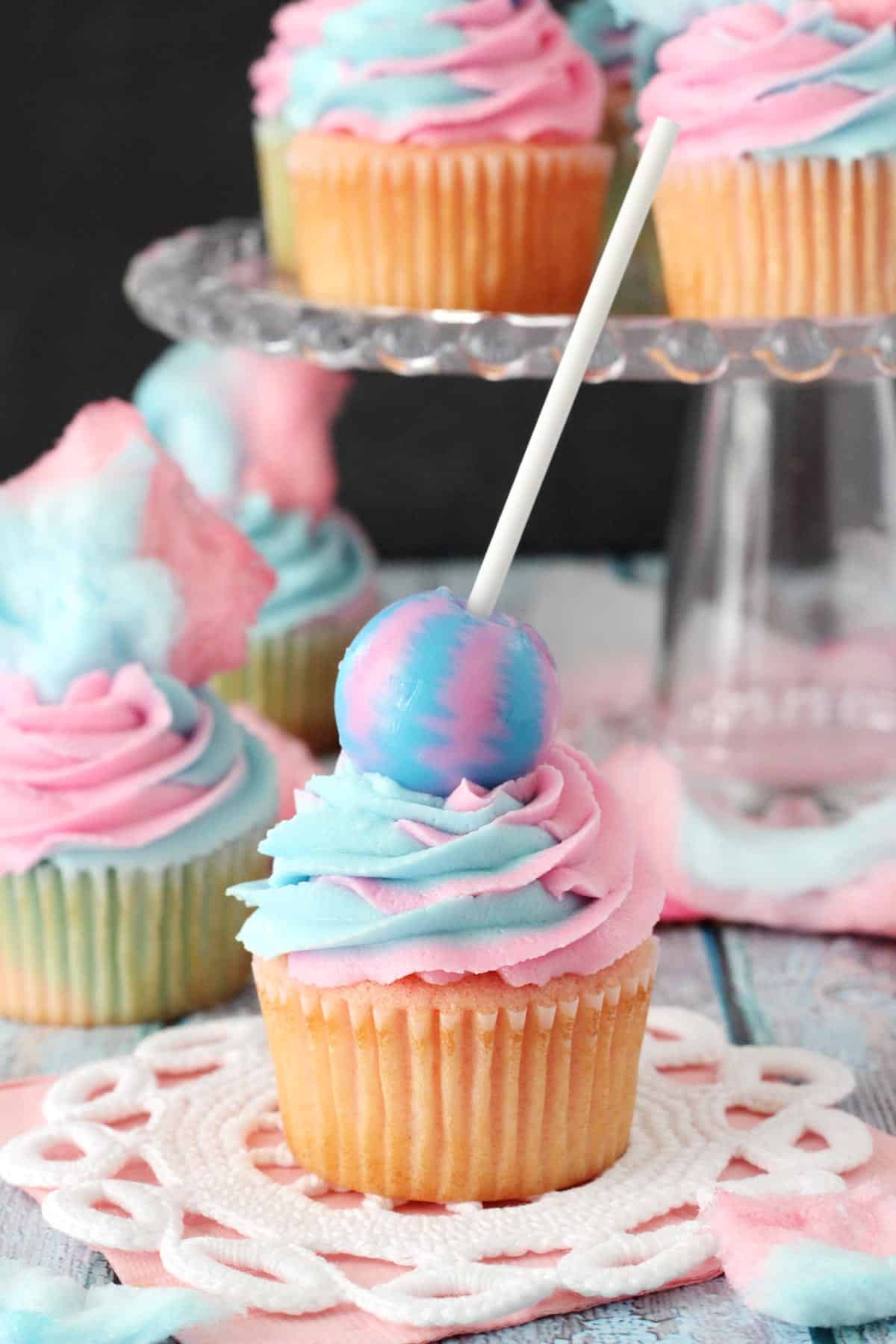 A cotton candy cupcake with a sucker on top.
