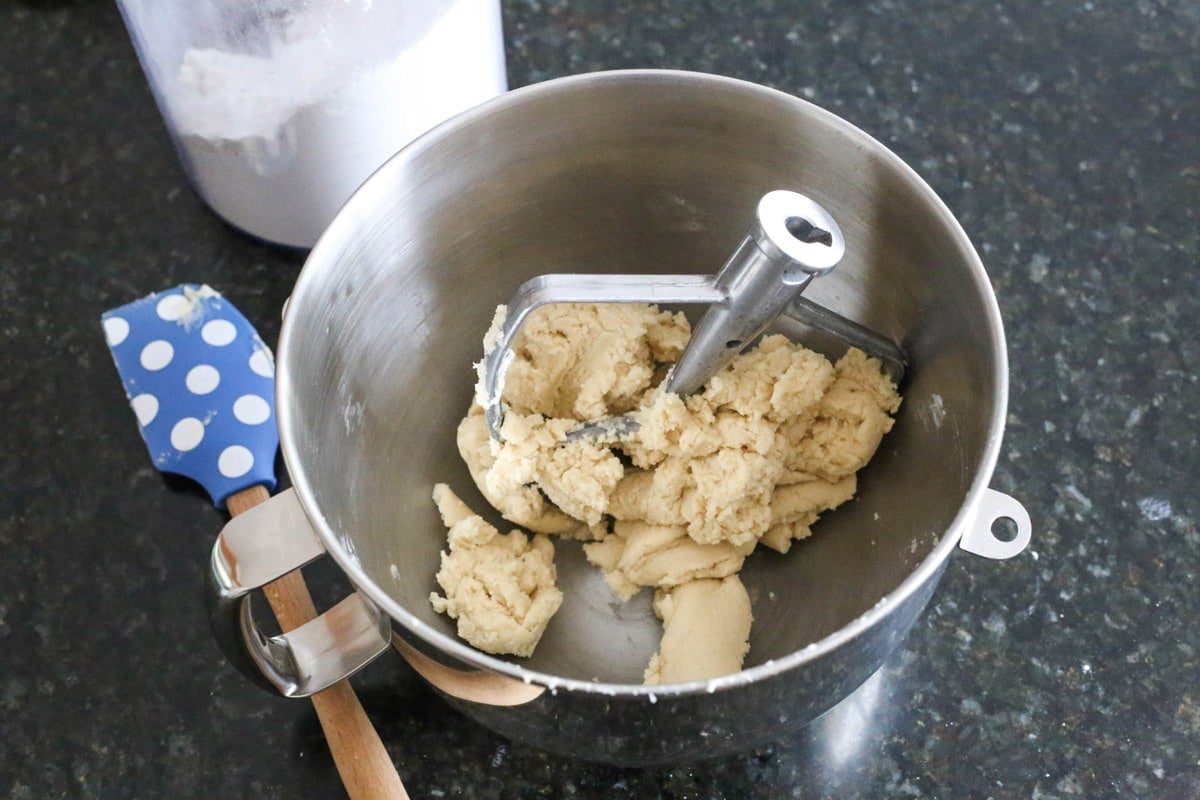 Sugar cookie dough in a mixer bowl next to a spatula.