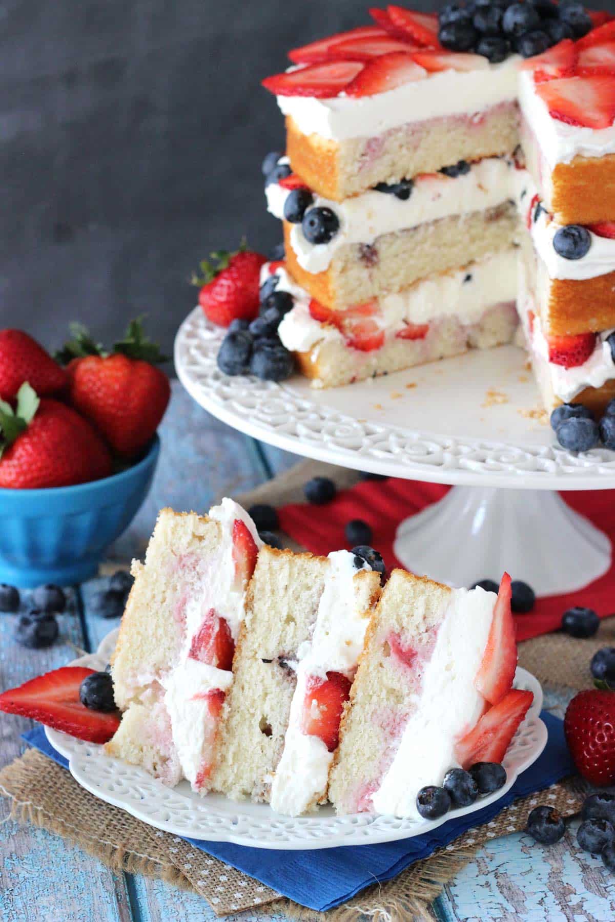 A slice of fresh berry vanilla layered cake on a small white plate with the rest of the cake in the background.