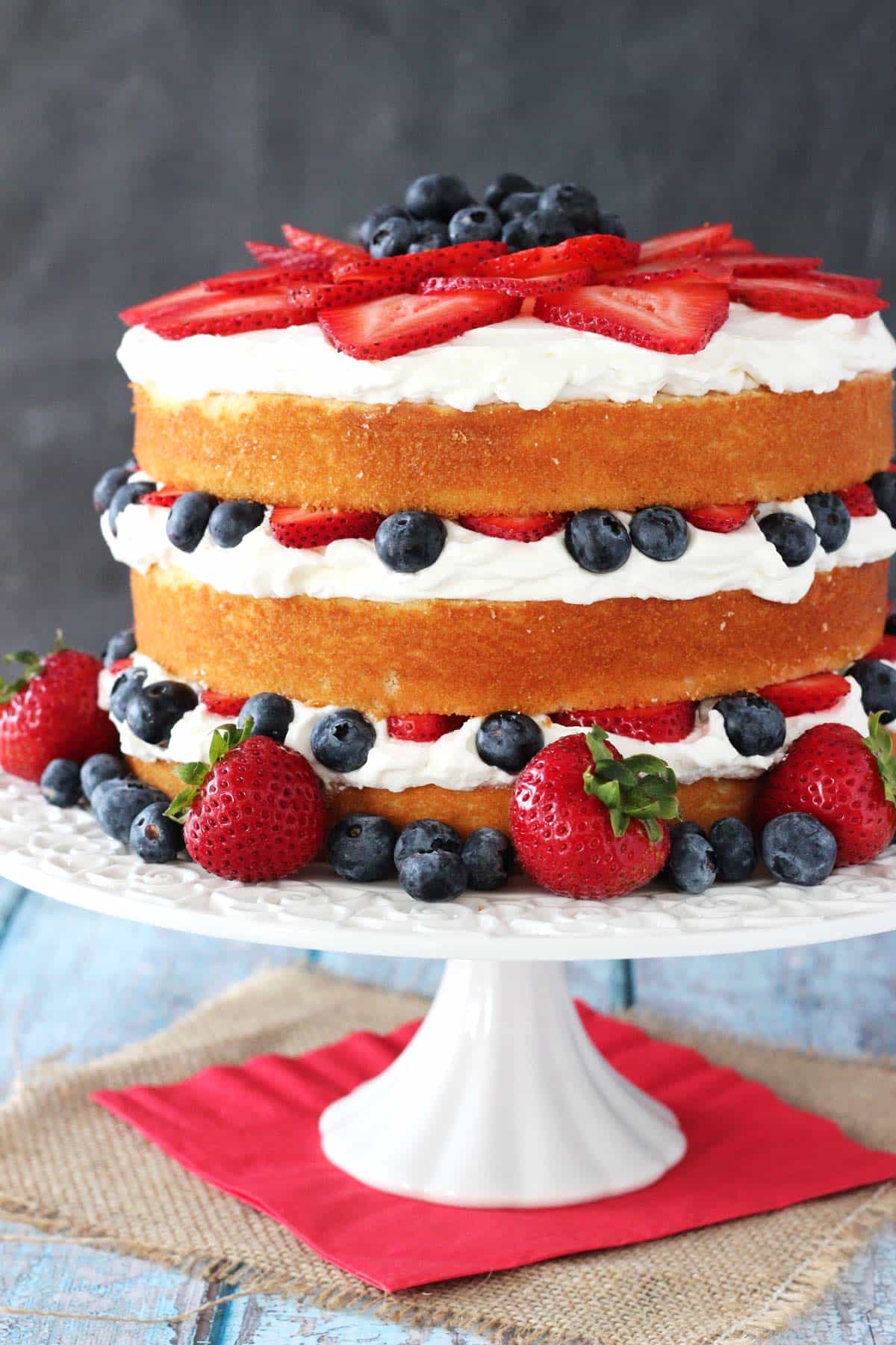 A fresh berry vanilla layered cake on a white cake stand.