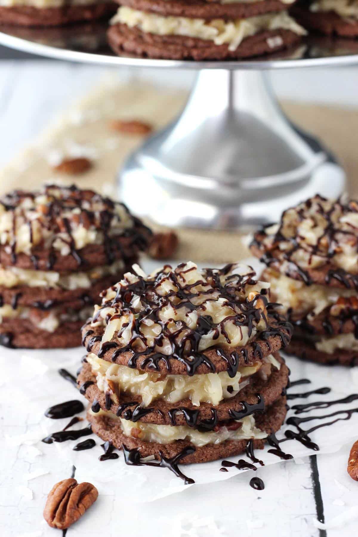 A few German chocolate cookie stacks with a cake plate in the background.