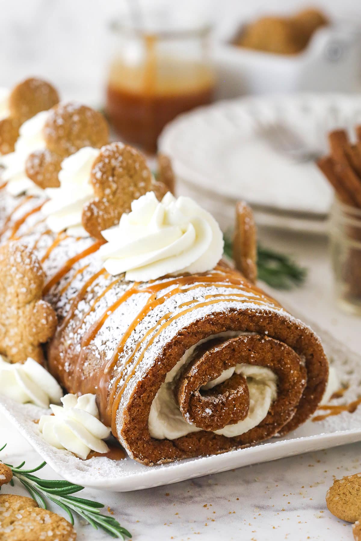 Gingerbread cake roll is a fun alternative to the classic, featuring a moist, spiced cake wrapped around a caramel and cream cheese filling. Christmas cake roll decorated with cream cheese whipped cream and gingerbread men.