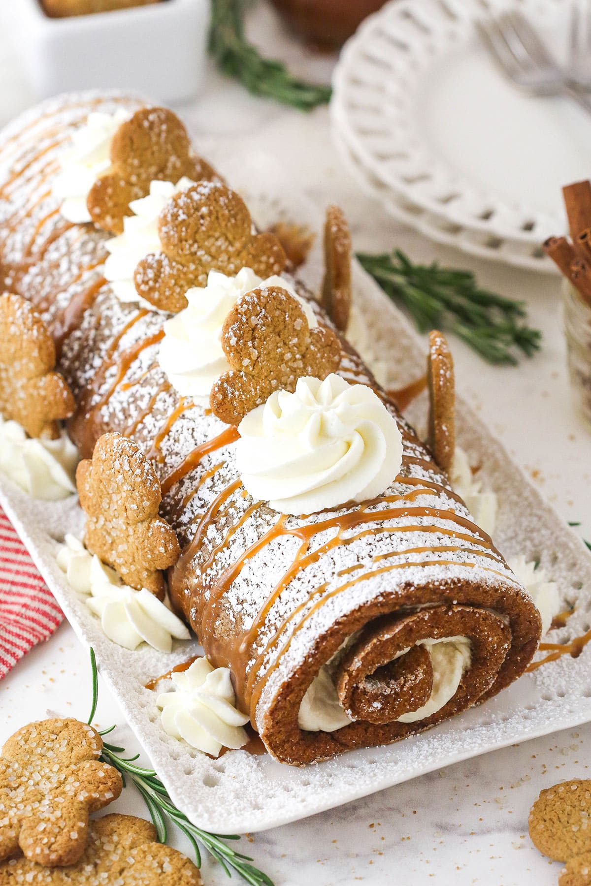Gingerbread cake roll is a fun alternative to the classic, featuring a moist, spiced cake wrapped around a caramel and cream cheese filling. Overhead image of gingerbread cake roll decorated with cream cheese whipped cream and gingerbread men.