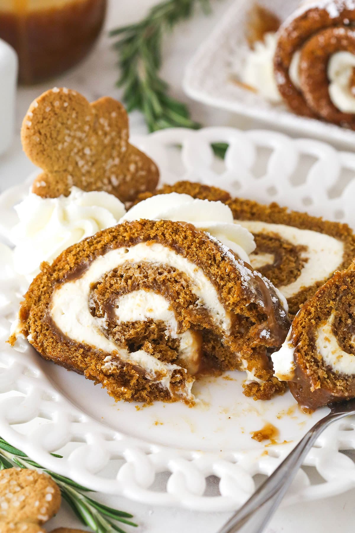 Gingerbread cake roll is a fun alternative to the classic, featuring a moist, spiced cake wrapped around a caramel and cream cheese filling. A couple of slices of gingerbread cake roll on a white plate.