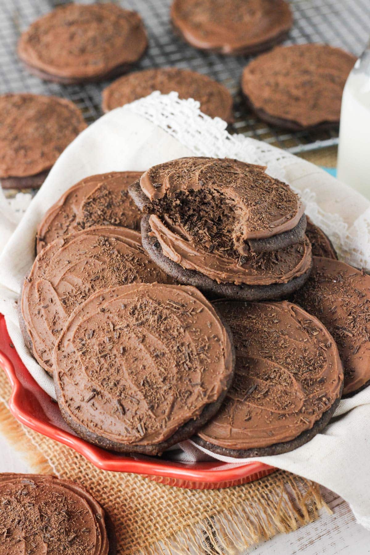 A pile of iced chocolate cookies on a plate with a bite taken out of the top cookie.