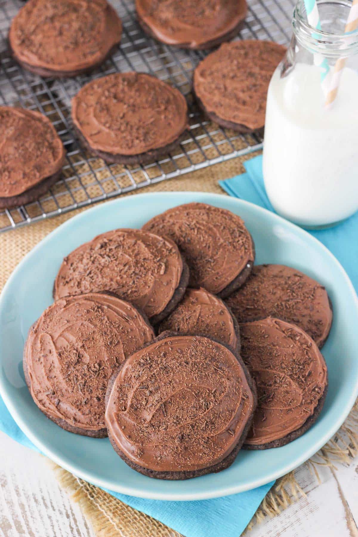 A plate of iced chocolate cookies next to a glass of milk.