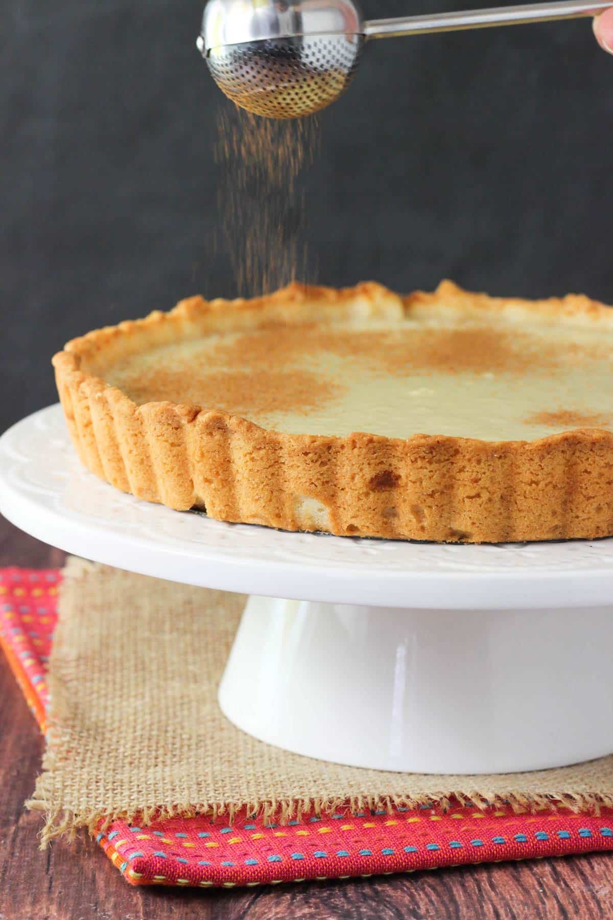 Sprinkling cinnamon over a milk tart.