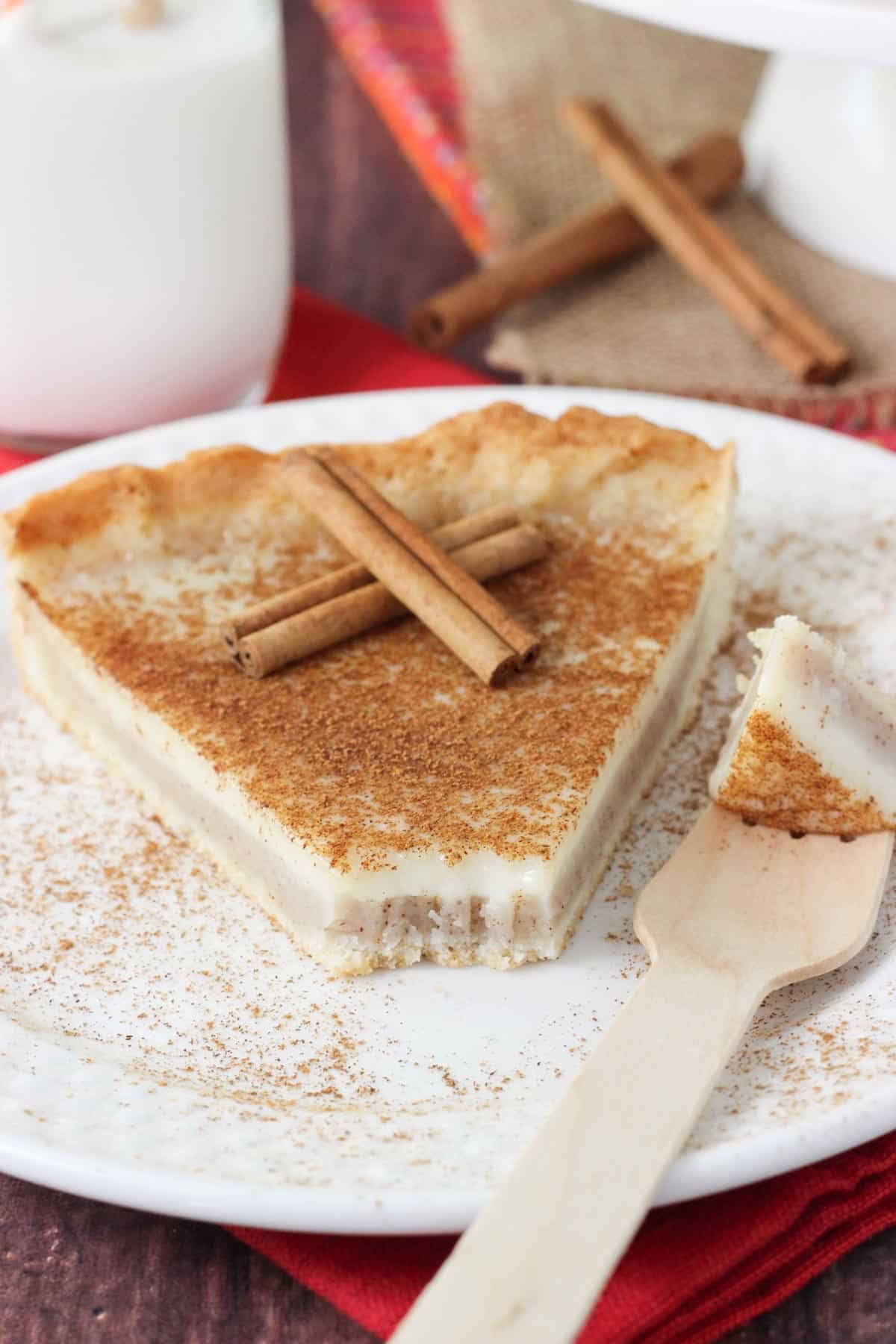 A slice of milk tart on a white plate with a bite removed on a fork.