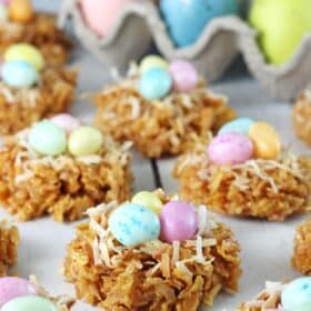 Close up of a no bake caramel coconut nest cookies with a carton of colorful eggs in the background.