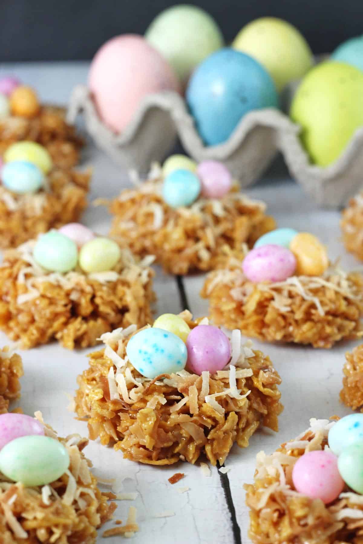 No Bake Coconut Caramel Nest Cookies Close up of a no bake caramel coconut nest cookies with a carton of colorful eggs in the background.