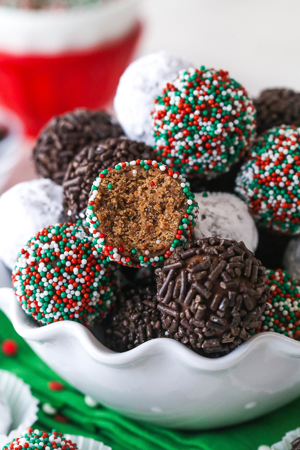 These customizable no-bake rum balls are a holiday must-have, perfect for gifting, gatherings, or adding to your festive cookie tray! Rum balls in a bowl. One has a bite taken out of it to reveal the center.