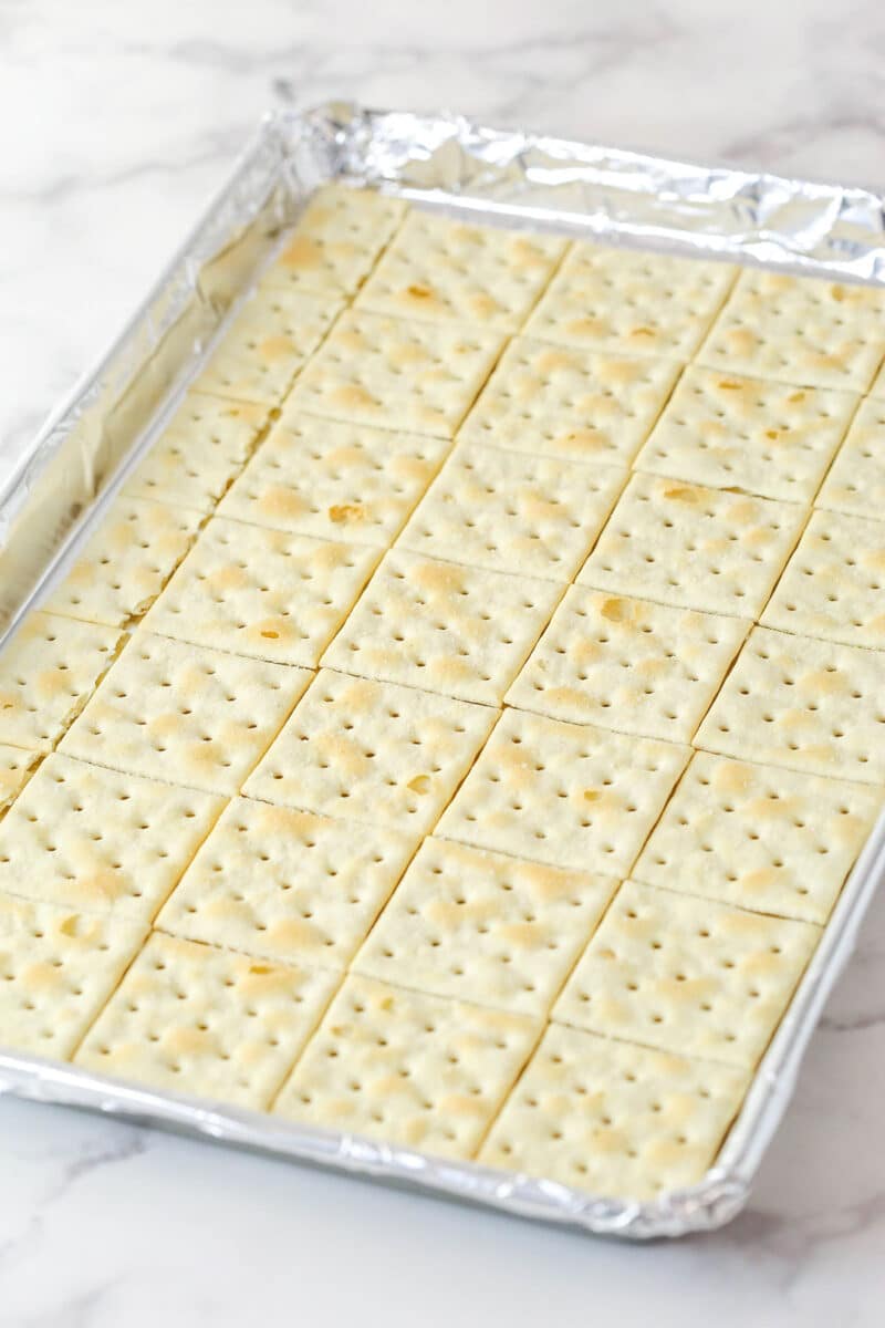 This saltine cracker toffee is rich, buttery, and full of crispy crackers. With a chocolate topping and crunchy pecans, it's a holiday must! Saltine crackers arranged in a single layer on a lined baking sheet.