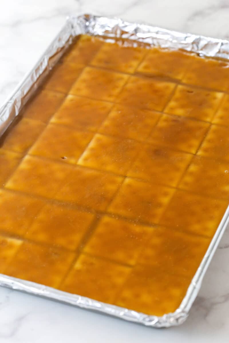 This saltine cracker toffee is rich, buttery, and full of crispy crackers. With a chocolate topping and crunchy pecans, it's a holiday must! Toffee poured over saltine crackers on a baking sheet.