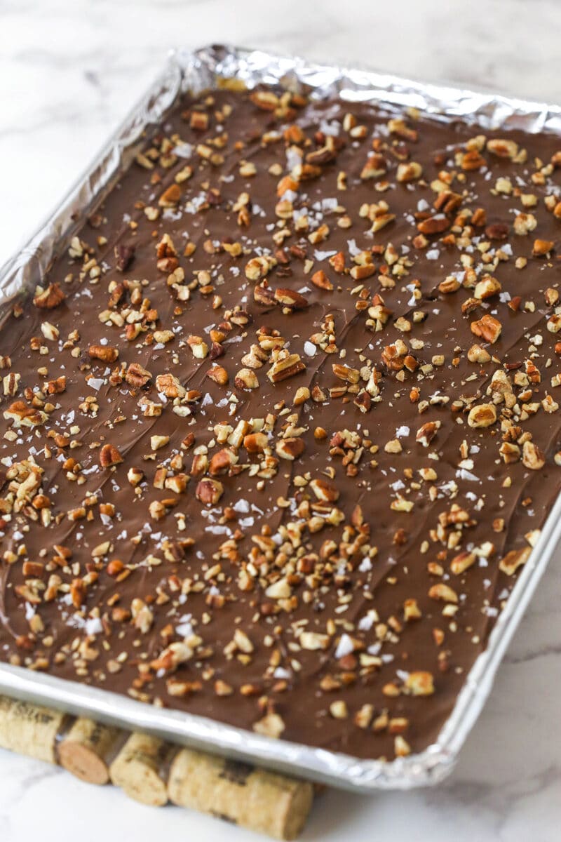 This saltine cracker toffee is rich, buttery, and full of crispy crackers. With a chocolate topping and crunchy pecans, it's a holiday must! Saltine cracker toffee cooling on a baking sheet.