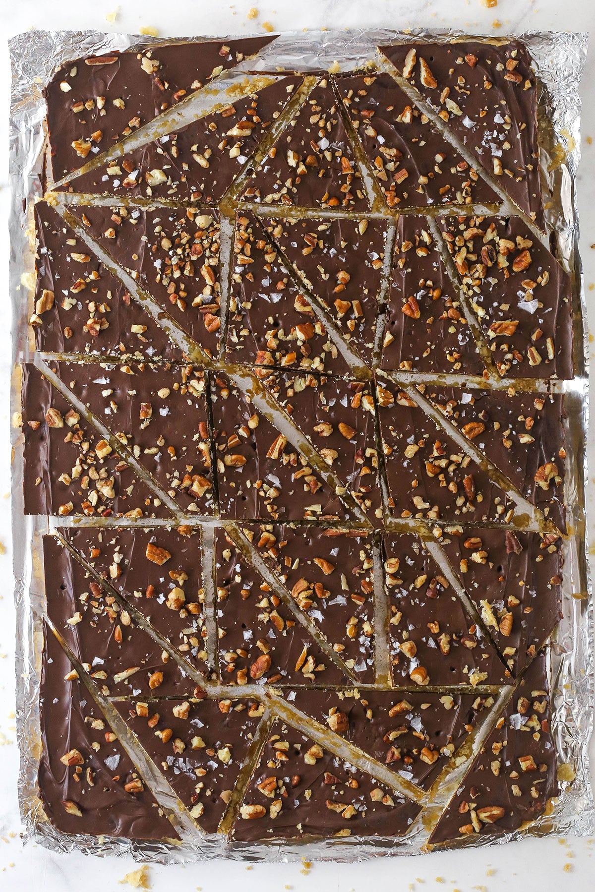 This saltine cracker toffee is rich, buttery, and full of crispy crackers. With a chocolate topping and crunchy pecans, it's a holiday must! Saltine cracker toffee broken into pieces on a aluminum foil-lined baking sheet.