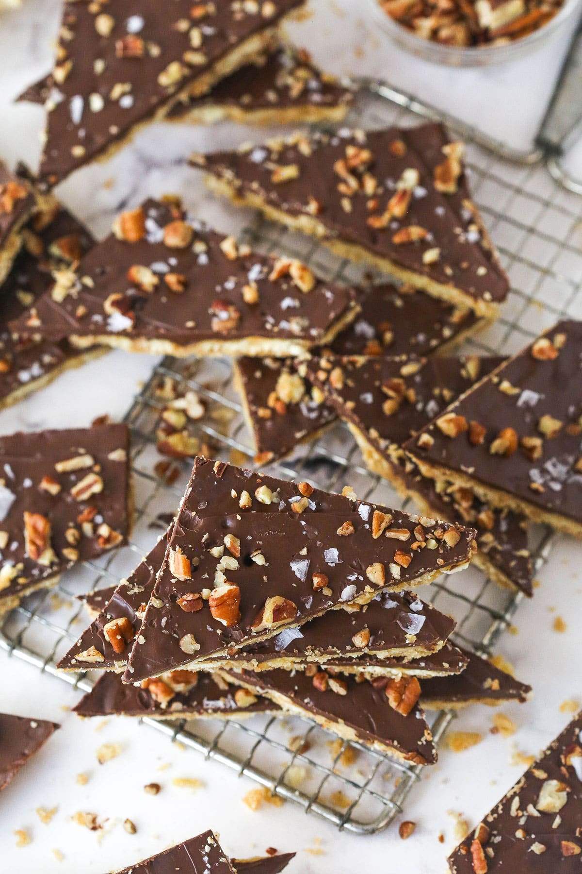 This saltine cracker toffee is rich, buttery, and full of crispy crackers. With a chocolate topping and crunchy pecans, it's a holiday must! Saltine cracker toffee broken into pieces on a cooling rack.