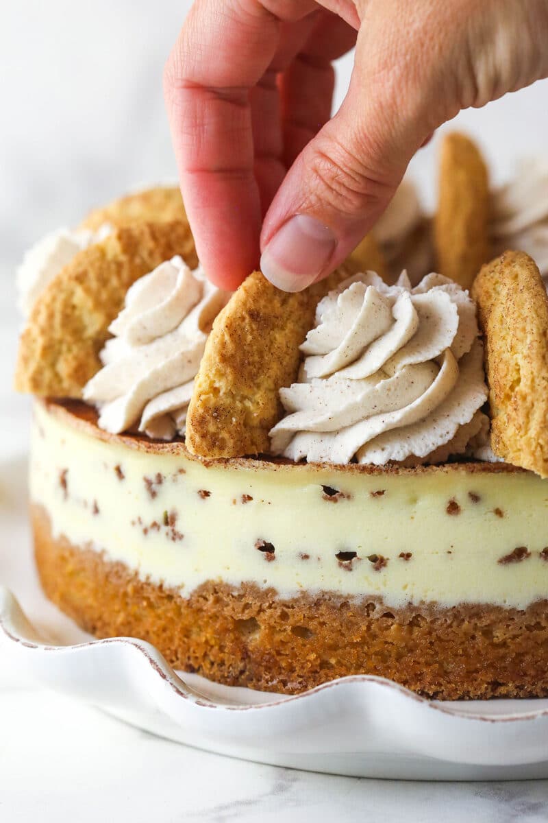 Placing halved snickerdoodles between swirls of cinnamon whipped cream on a snickerdoodle cheesecake.