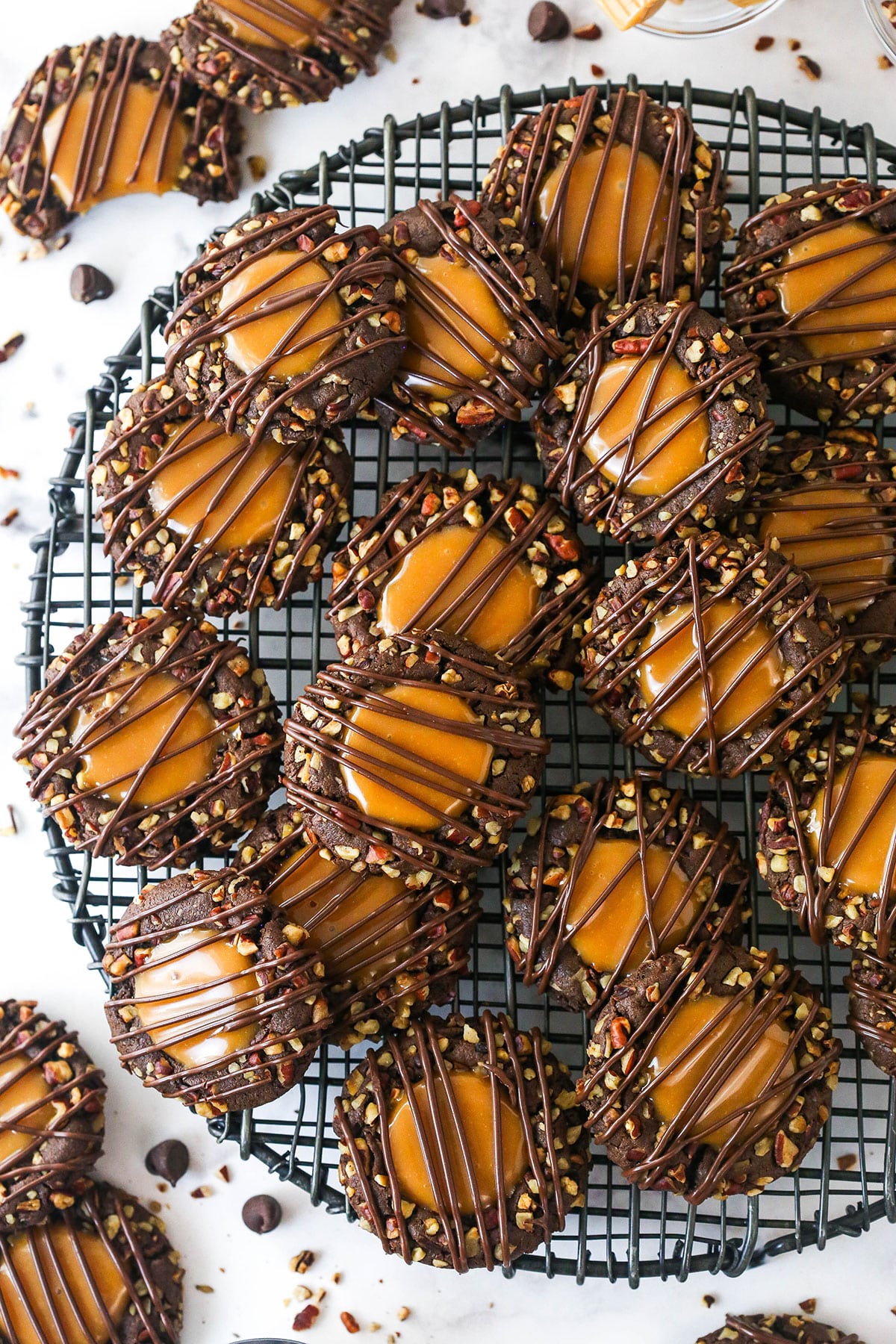 These decadent turtle thumbprint cookies feature a rich chocolate base, gooey caramel center, and crunchy pecan coating. Wow! Overhead image of turtle thumbprint cookie on a cooling rack.