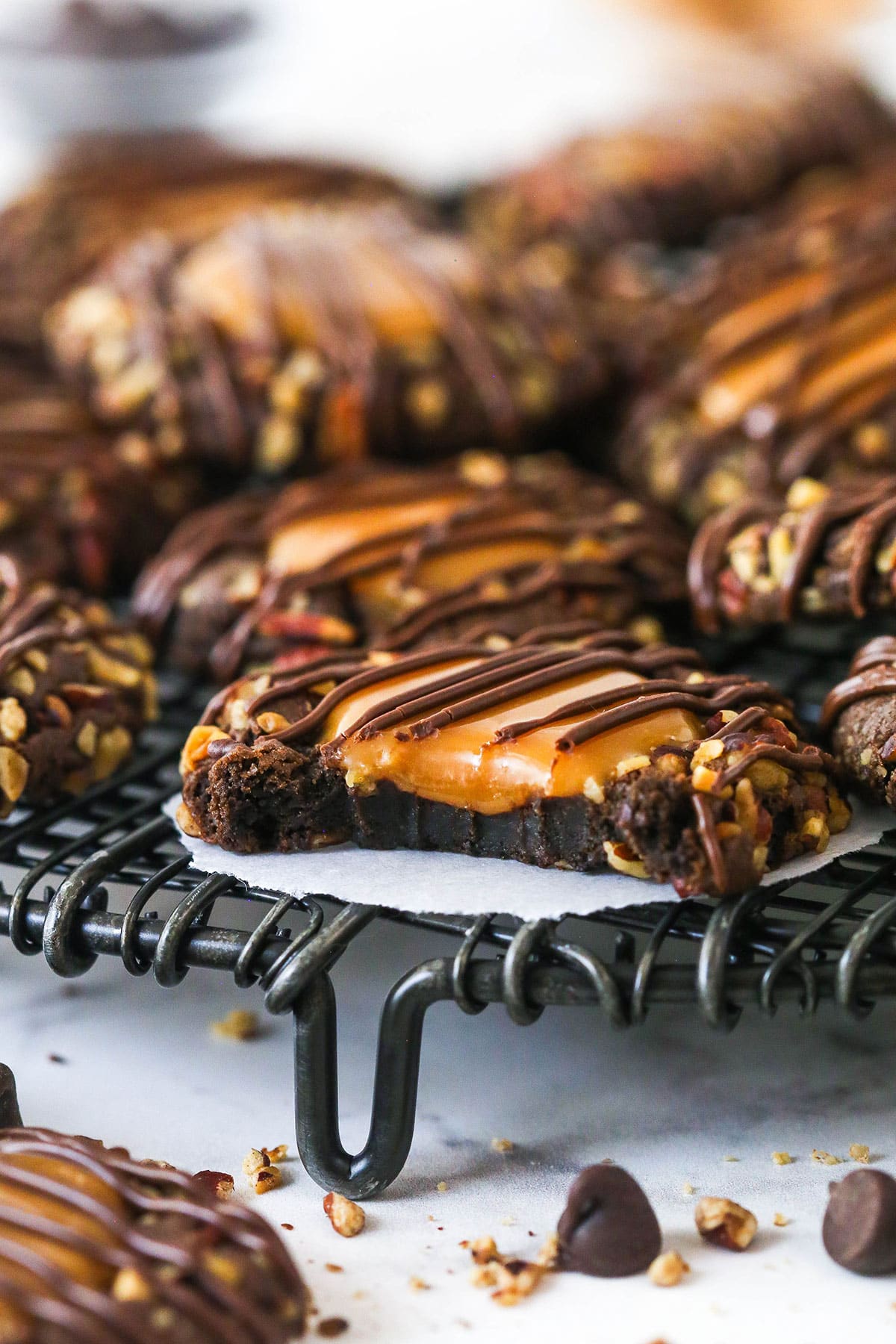 These decadent turtle thumbprint cookies feature a rich chocolate base, gooey caramel center, and crunchy pecan coating. Wow! Turtle thumbprint cookie on a cooling rack. One has a bite taken out of it.