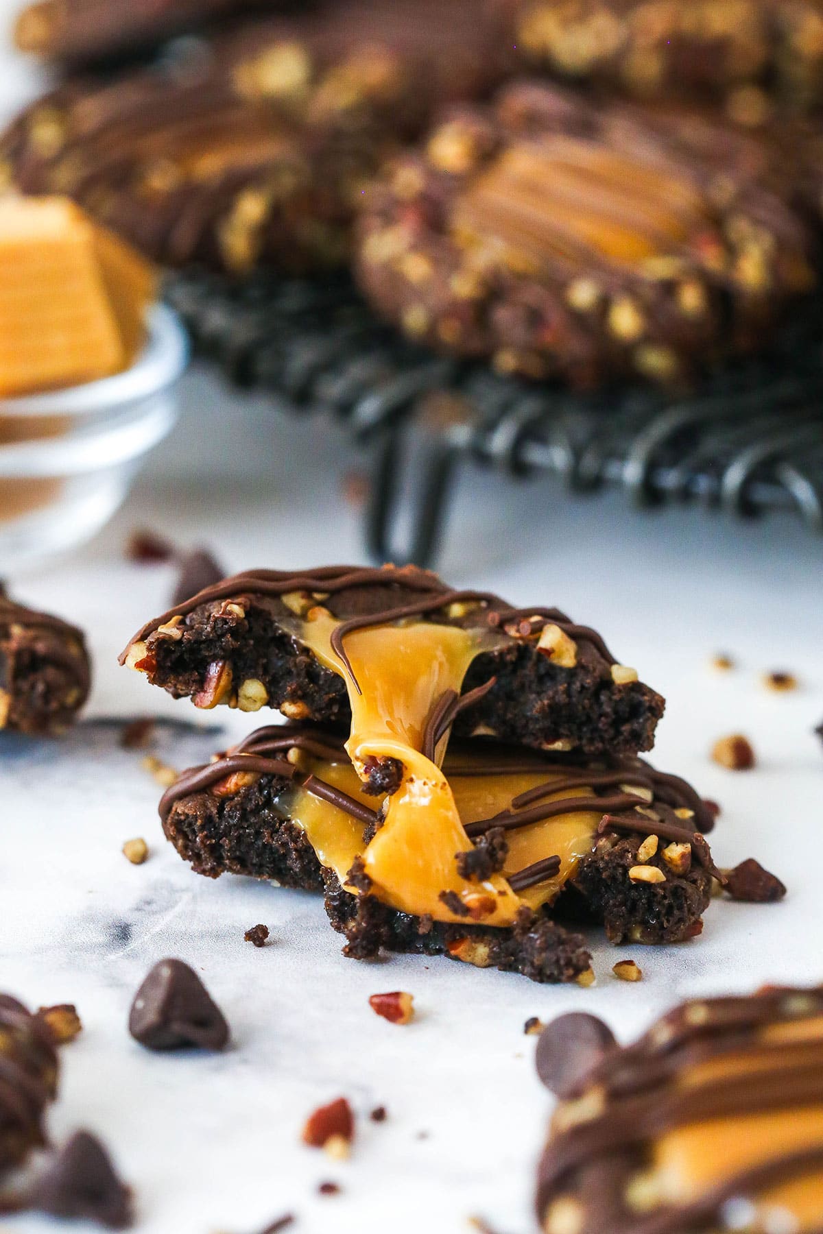 These decadent turtle thumbprint cookies feature a rich chocolate base, gooey caramel center, and crunchy pecan coating. Wow! A turtle thumbprint cookie broken in half.