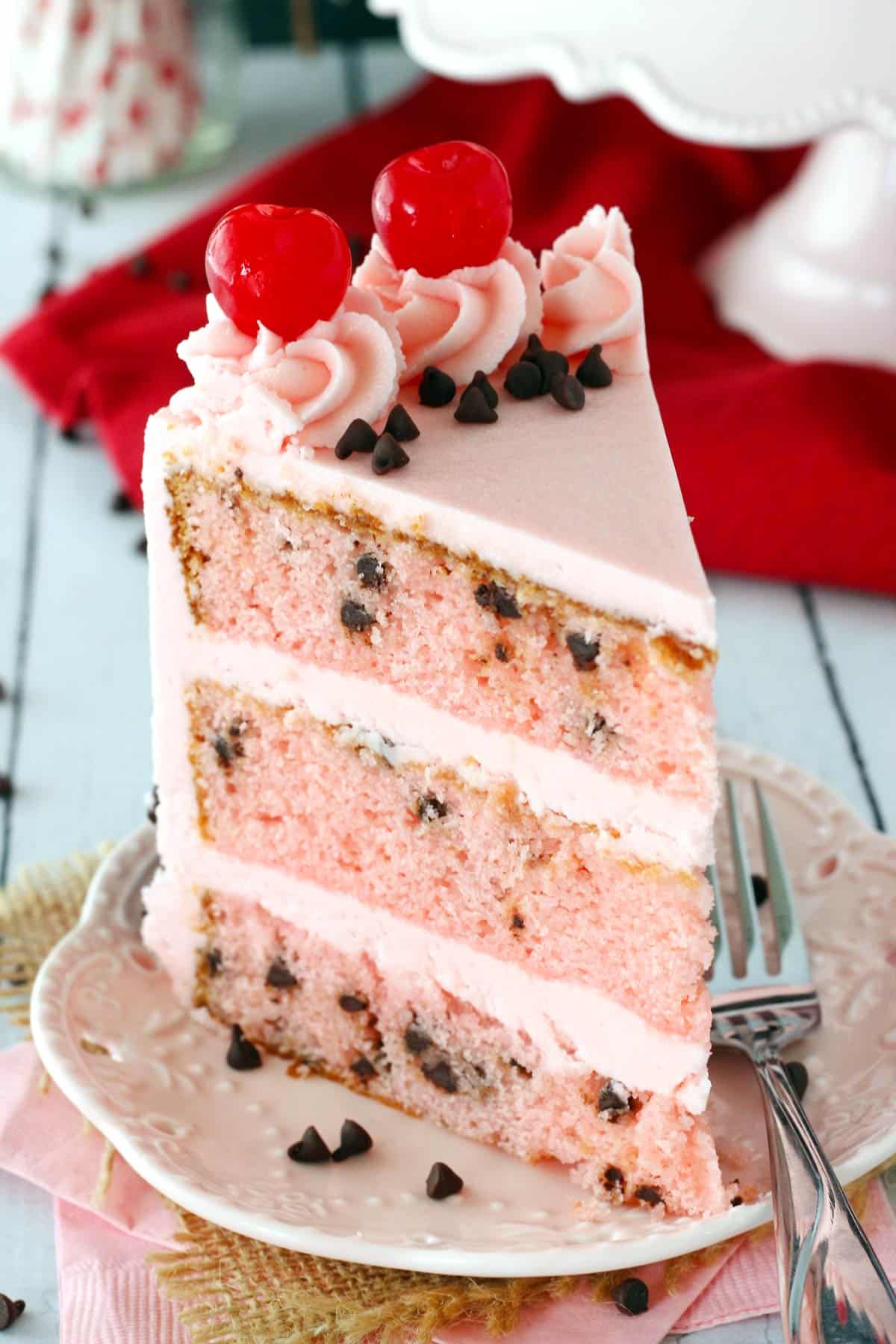 A tall slice of cherry chocolate chip cake on a white plate.