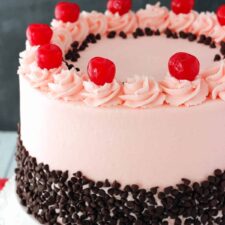 Close up of a cherry chocolate chip cake on a white cake stand.