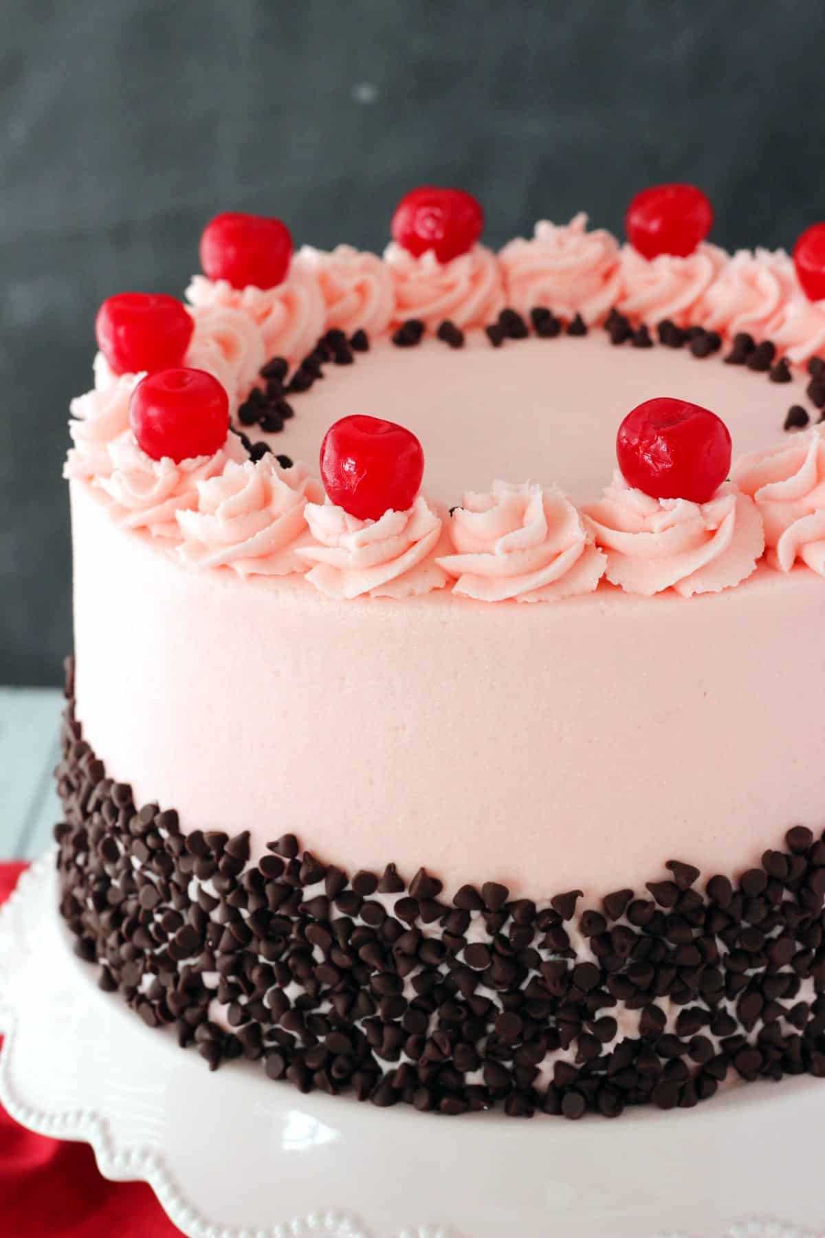 Close up of a cherry chocolate chip cake on a white cake stand.