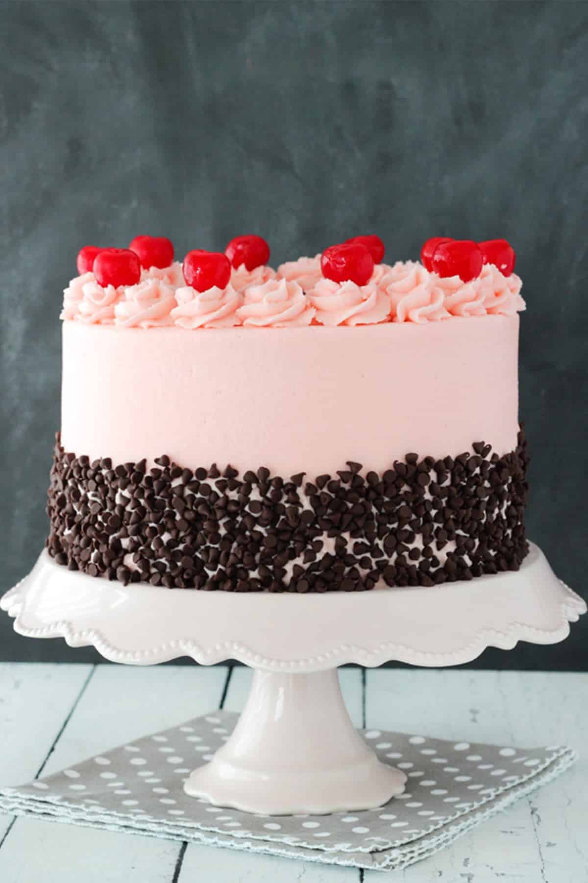 A cherry chocolate chip cake on a white cake stand.