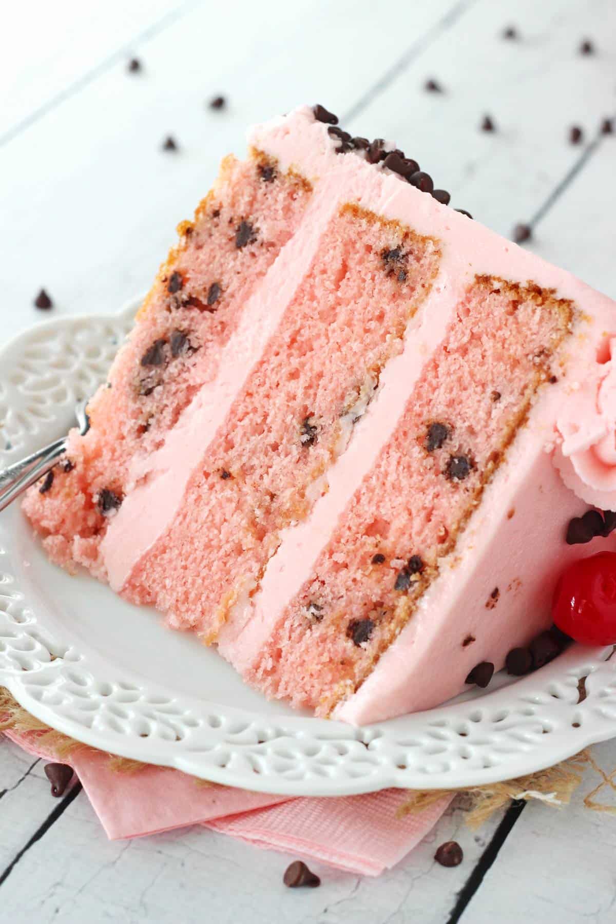 A slice of cherry chocolate chip cake on a white plate.
