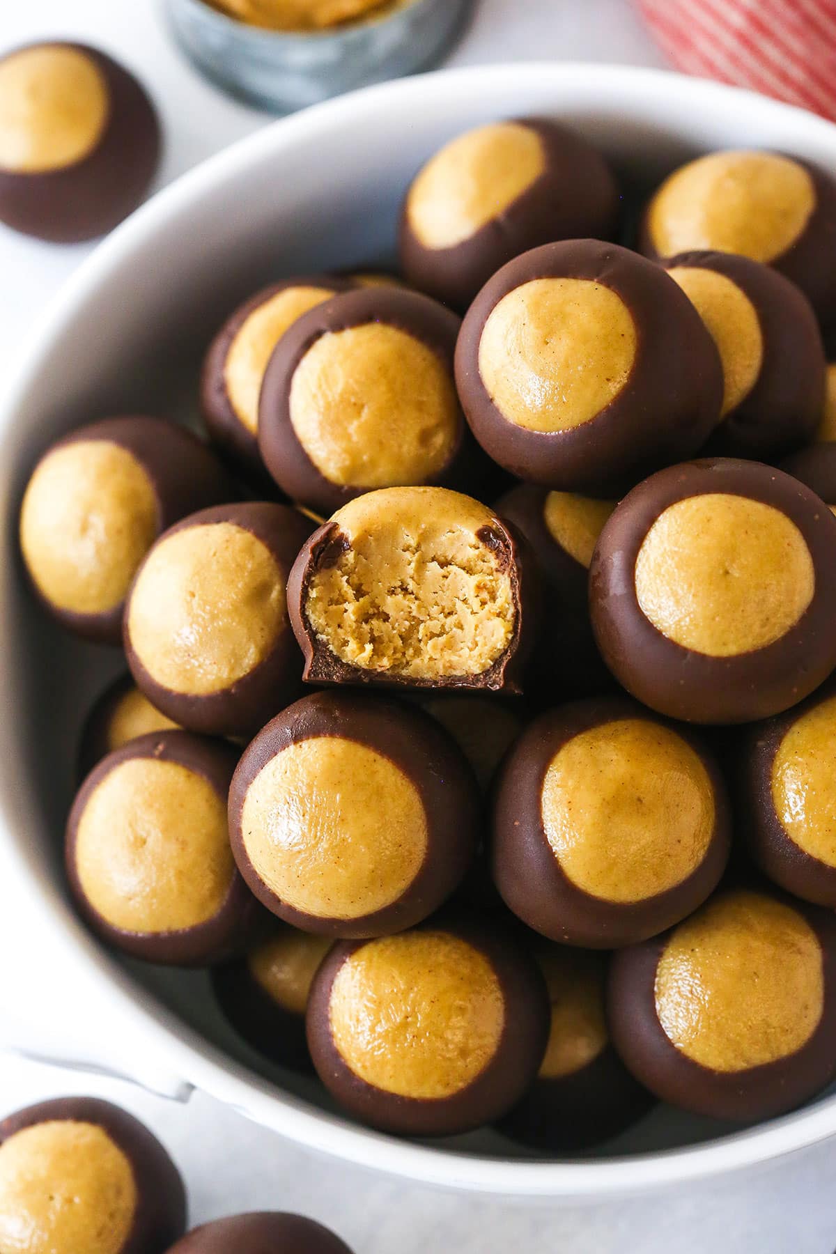 These Buckeyes have the perfect smooth and creamy texture with a sweet, nutty peanut butter and chocolate flavor. No baking required! Overhead view of a bowl of buckeyes with one missing a bite to show the creamy inside