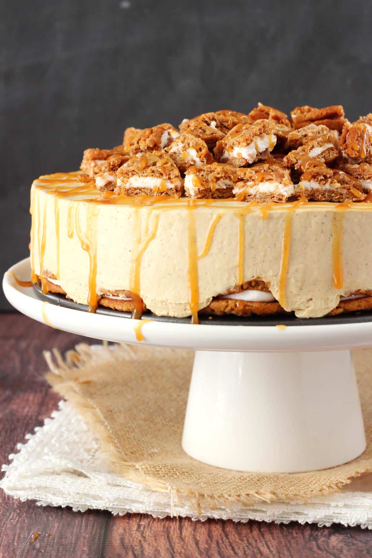 Side view of a no bake oatmeal cream pie cheesecake on a white cake stand.