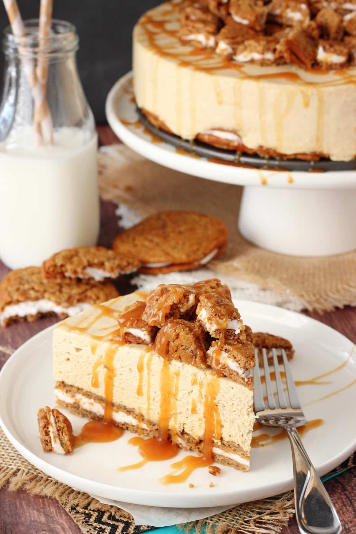 A slice of no bake oatmeal cream pie cheesecake on a white plate with the rest of the cheesecake in the background.
