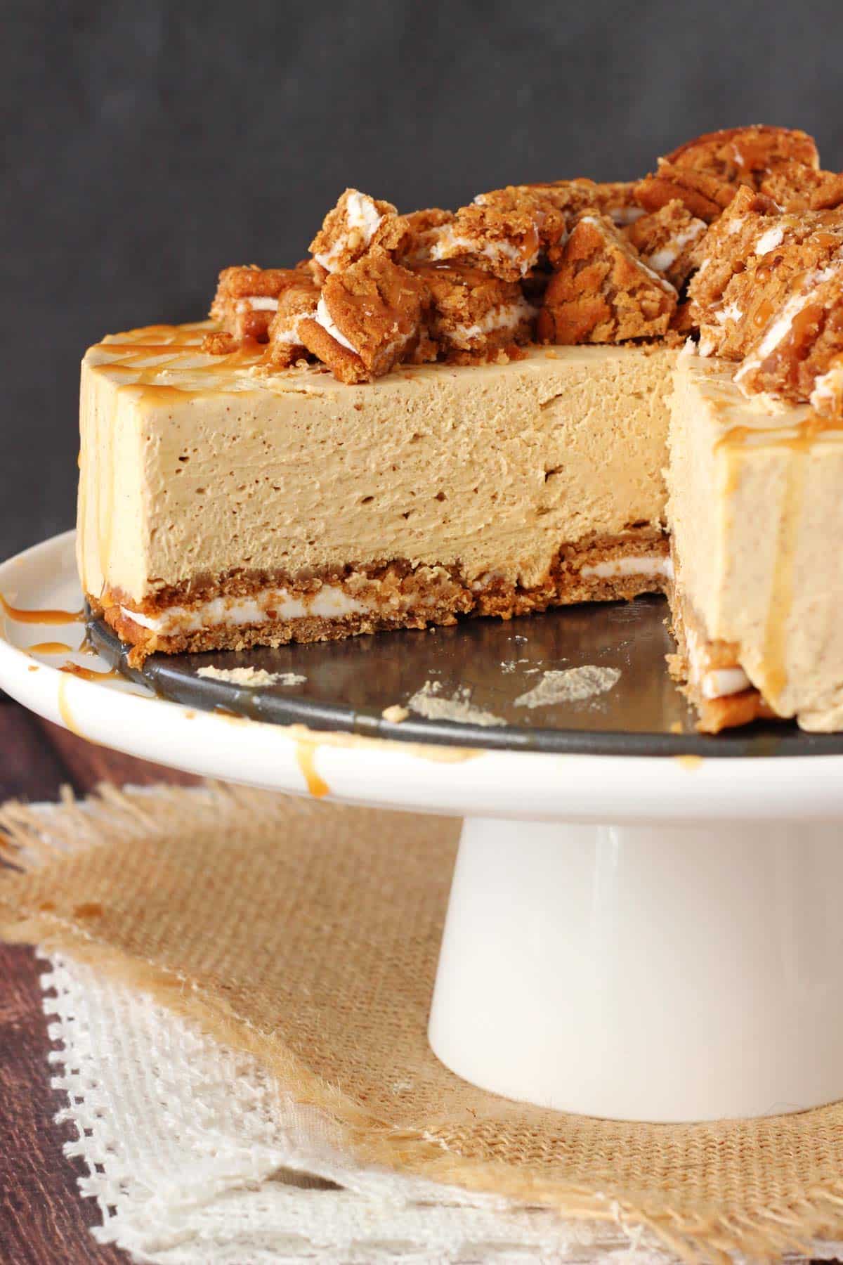 Close up of a no bake oatmeal cream pie cheesecake on a white cake stand with a slice removed to show layers.