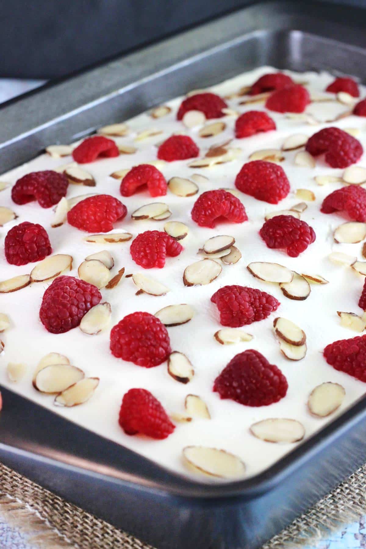 A raspberry almond poke cake in a metal baking pan.
