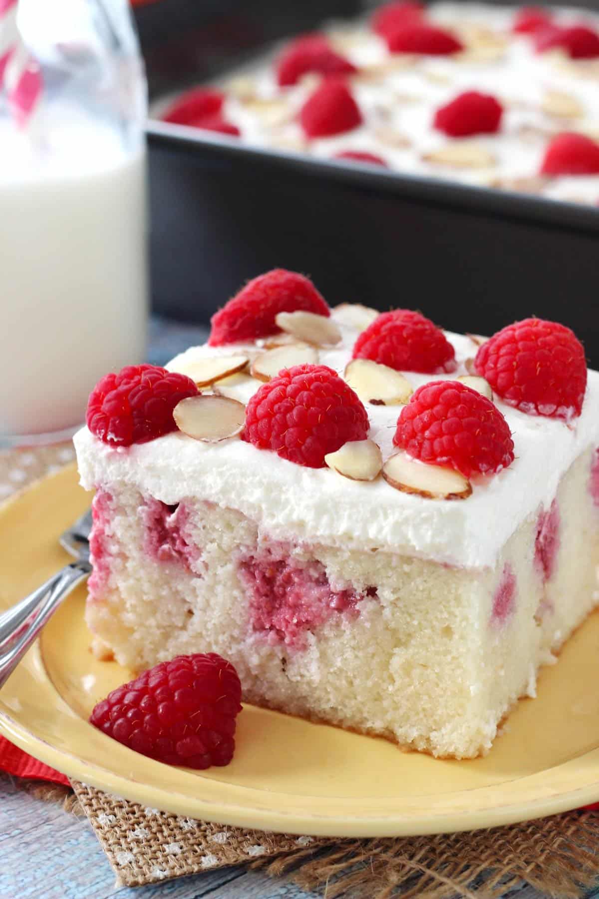A slice of raspberry almond poke cake on a yellow plate.