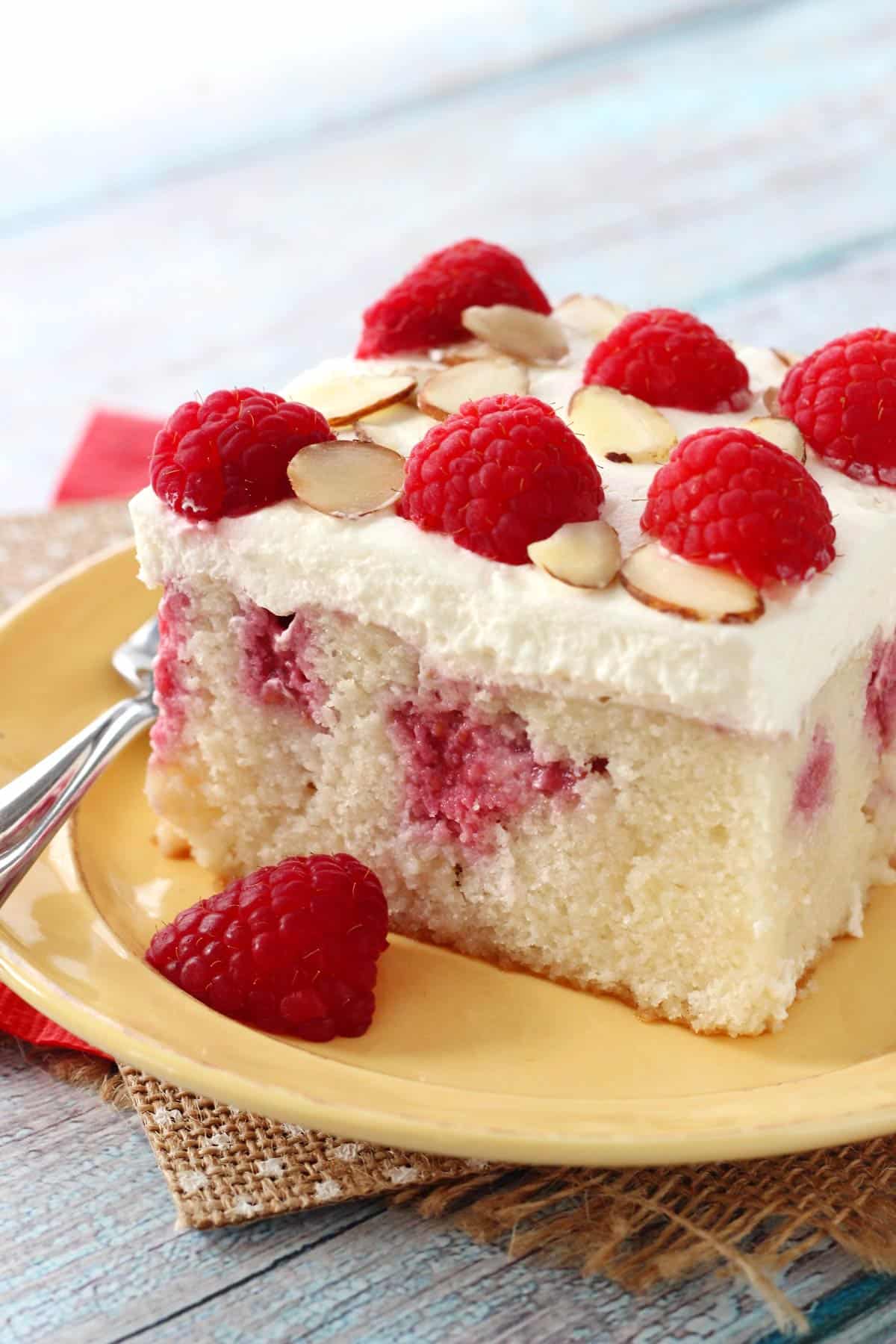 Close up of a slice of raspberry almond poke cake on a yellow plate.