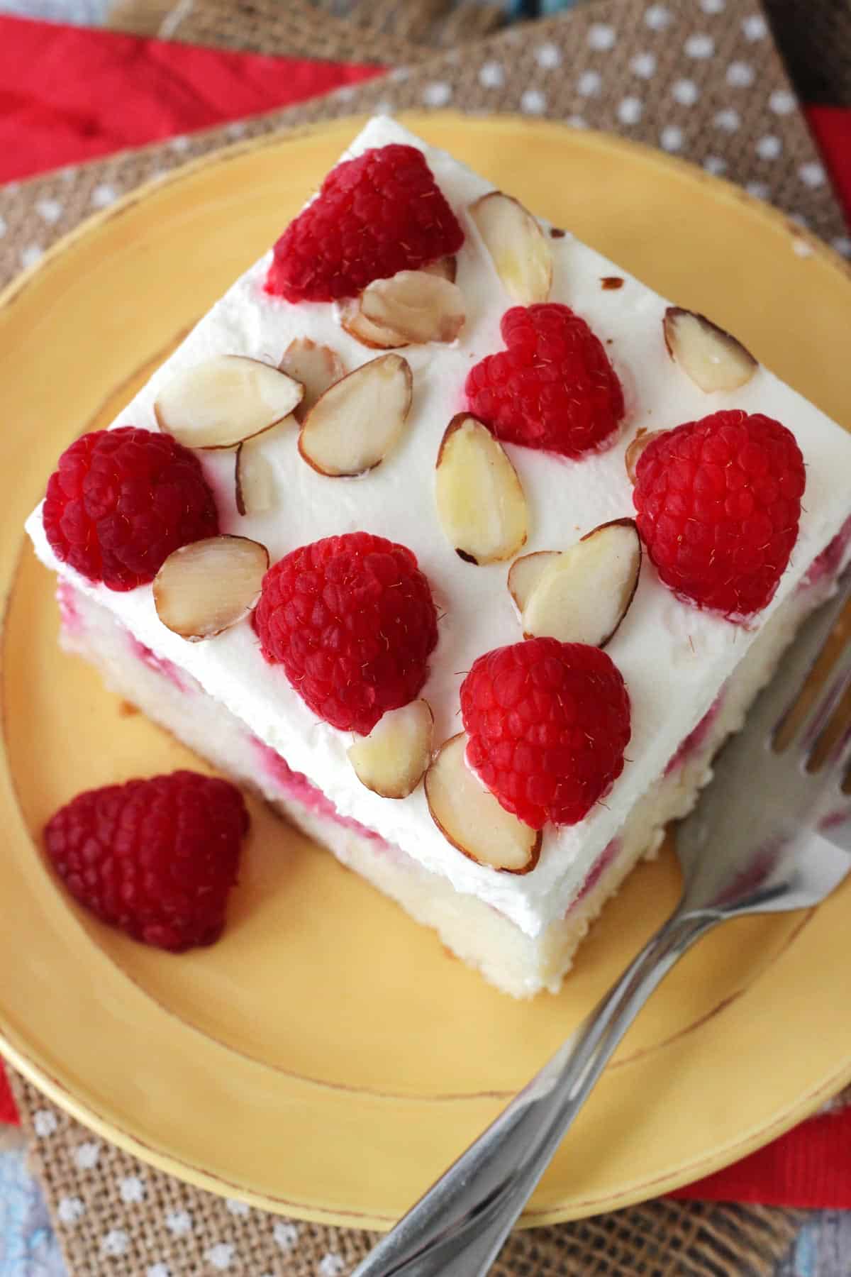 Top view of a slice of raspberry almond poke cake on a yellow plate.