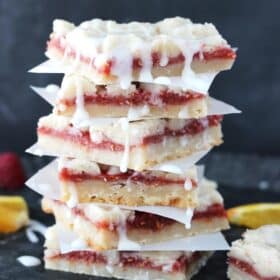A tall stack of raspberry orange shortbread bars separated by pieces of parchment.
