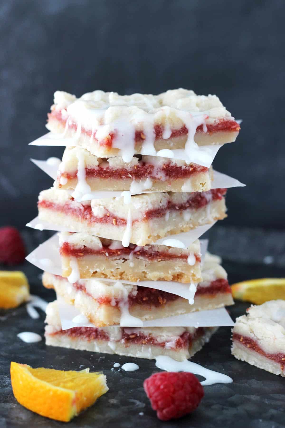 A tall stack of raspberry orange shortbread bars separated by pieces of parchment.