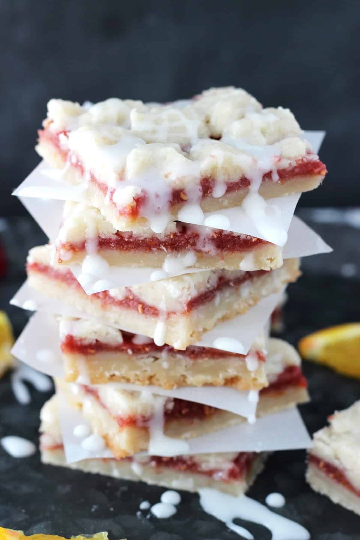 A tall stack of raspberry orange shortbread bars separated by parchment squares.