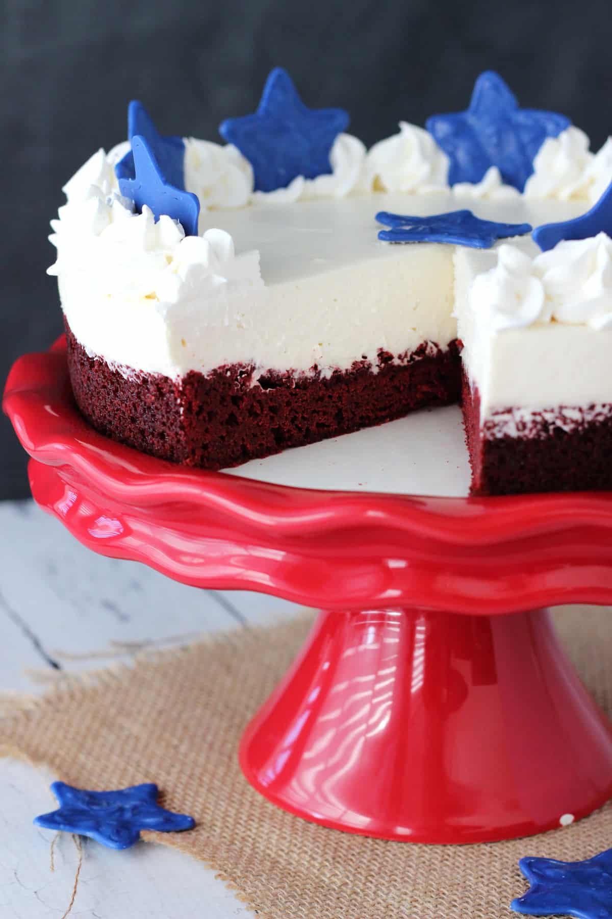 A red velvet blondie cheesecake on a red cake stand with a slice removed to show interior.