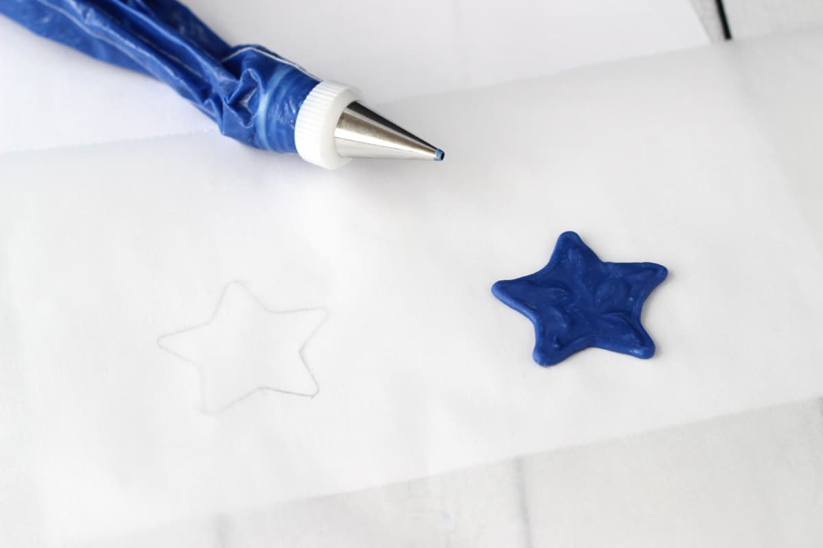 A blue star made from candy coating on a piece of parchment next a piping bag.
