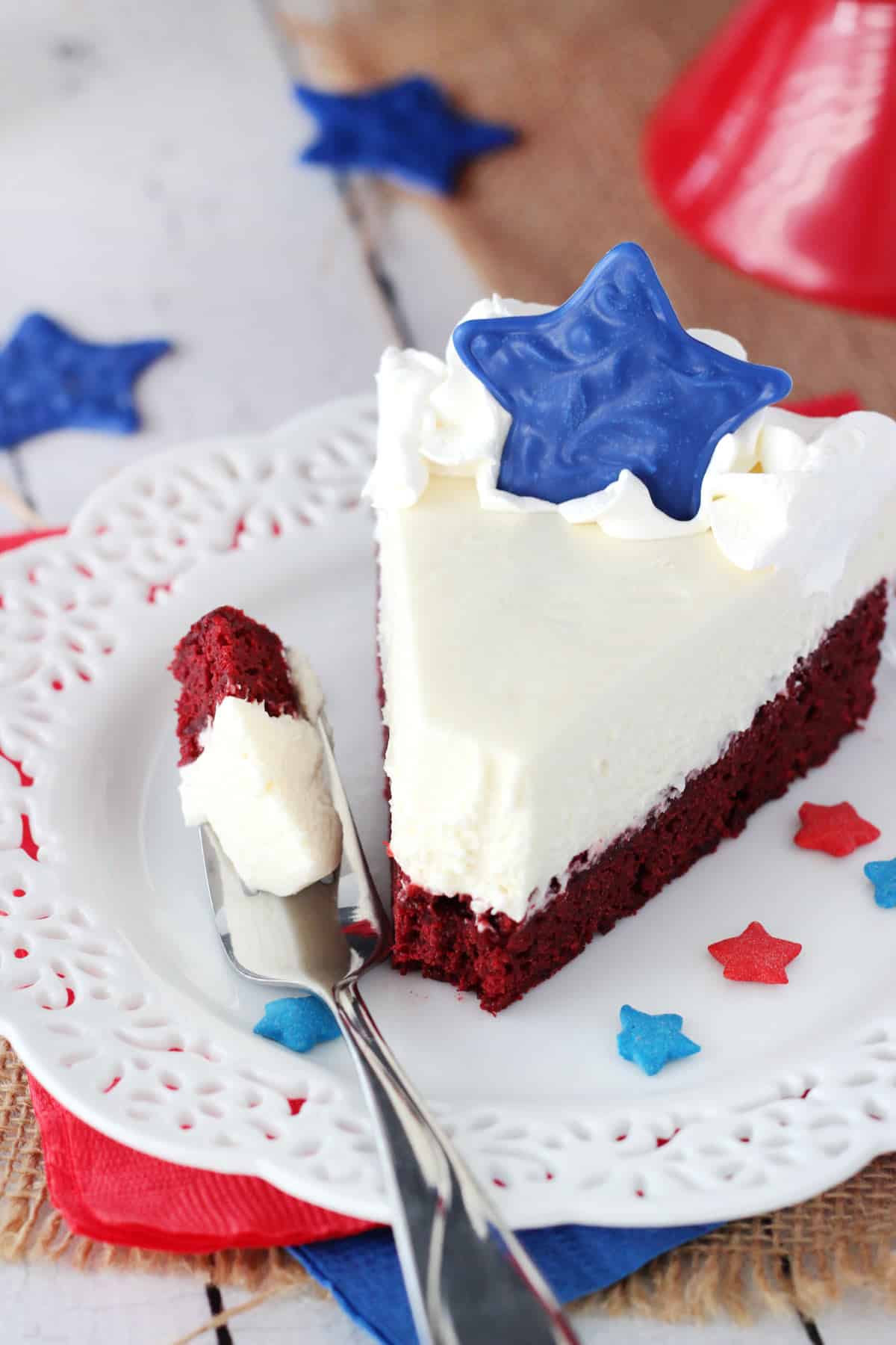 A slice of red velvet blondie cheesecake on a small white plate with a bite removed on a fork.