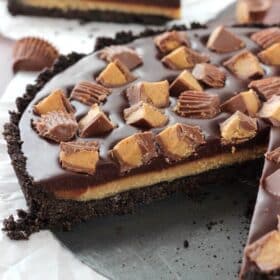 A Reese's chocolate peanut butter tart with a slice missing to show layers.