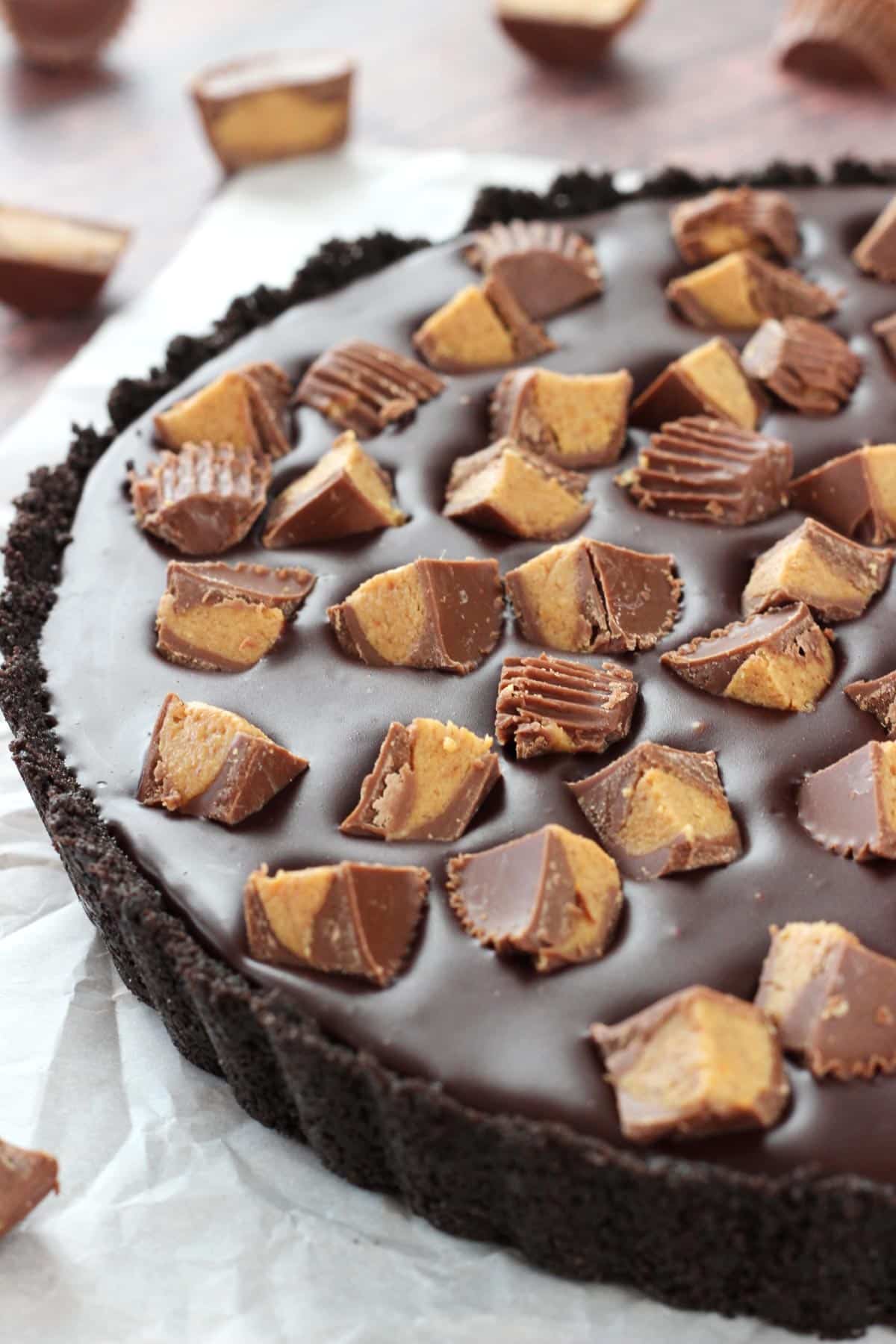 A Reese's chocolate peanut butter tart covered with peanut butter cups on a piece of parchment paper.