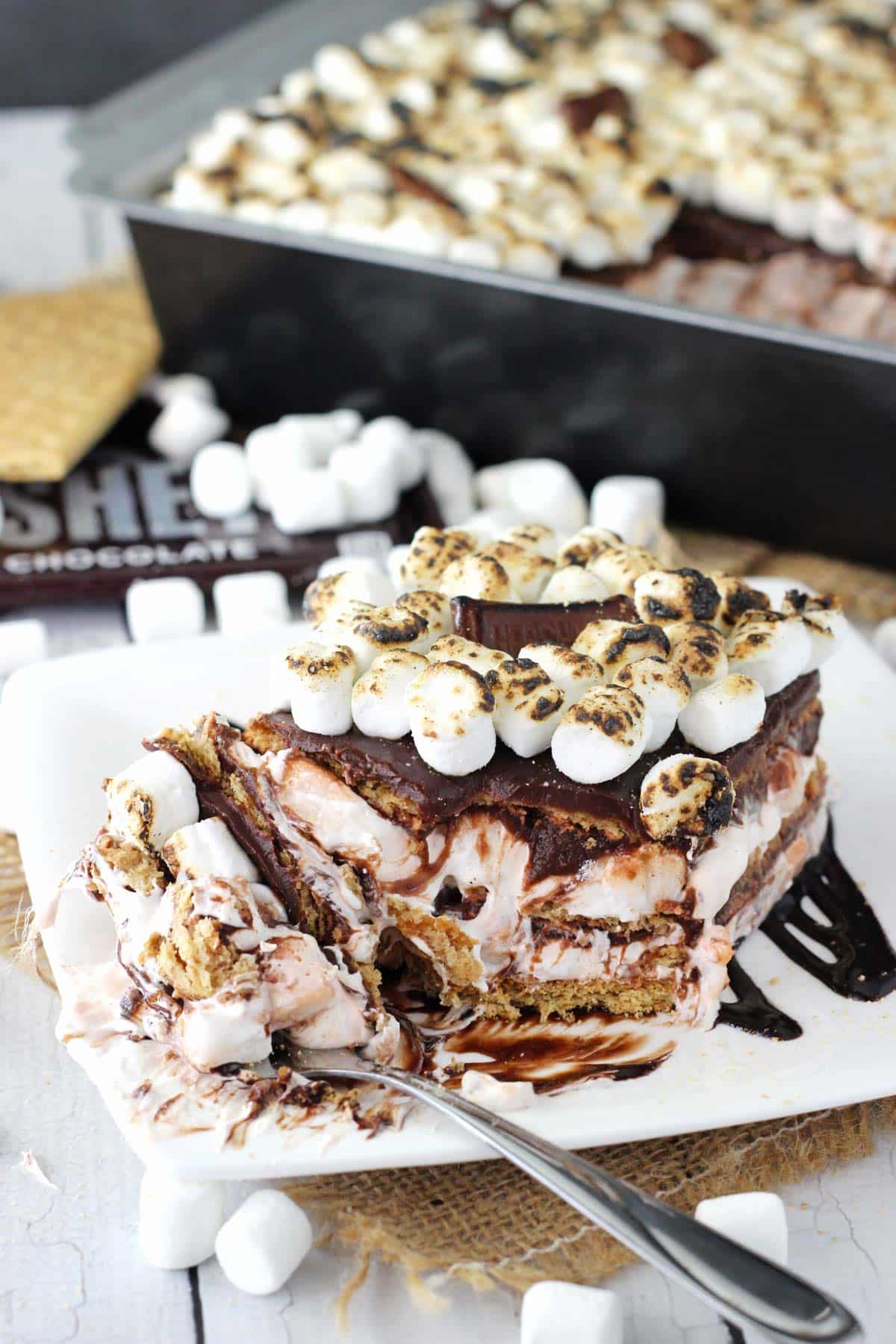 A slice of smores icebox cake on a white plate with a few bites removed on a fork.